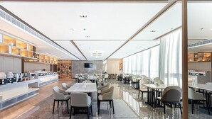 En moderne restaurant med en lang bardisk, flere borde og et højtloft med indbygget belysning.
