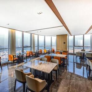 Een restaurant in een hoog gebouw met grote ramen die uitzicht over de stad bieden, modern meubilair en een glanzende vloer.