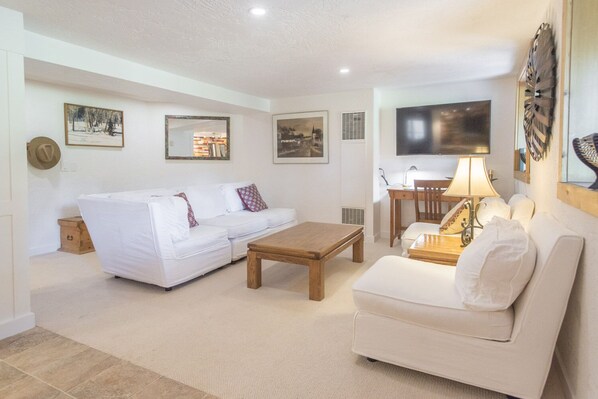 A living room with a white sofa, a wooden coffee table, and a TV mounted on the wall. - Best Deal, small 2 bedroom unit (Ketchum)