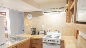 A compact kitchen with wooden cabinets, a built-in stove, a sink, and a toaster. - Best Deal, small 2 bedroom unit (Ketchum)