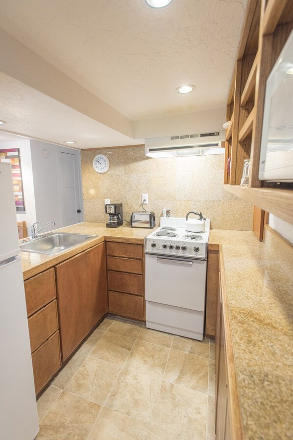 A compact kitchen with wooden cabinets, a built-in stove, a sink, and a toaster.