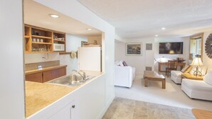 A modern kitchen with a built-in microwave, a sink, and wooden cabinets. Adjacent to the kitchen is a living area with a white sofa, a coffee table, and a TV. - Best Deal, small 2 bedroom unit (Ketchum)