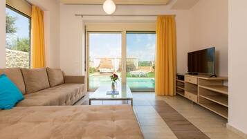 A modern living room with a sofa, coffee table, and TV. It features a sliding glass door leading to a pool area.
