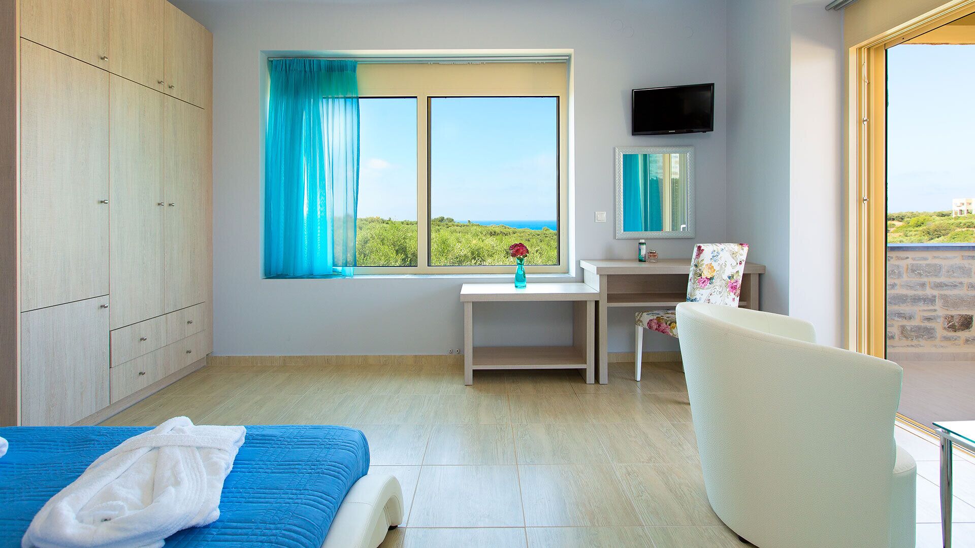A bedroom with a bed, a desk, a chair, a TV, and a window with a view.