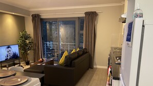 A modern living room with a sofa, dining table, and a television. - Tana’s Crib Modern Secure 1 bed apartment (Cape Town)