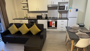 A modern kitchen with a dining area, featuring a sofa with cushions, a dining table with plates, and a microwave. - Tana’s Crib Modern Secure 1 bed apartment (Cape Town)
