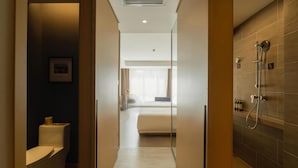 A hotel bathroom with a shower, toilet, and a bed visible through a glass door. - Atour Hotel (Changchun)