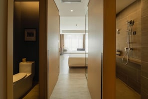 Une salle de bain d’hôtel équipée d’une douche, de toilettes et d’un lit visible à travers une porte en verre.