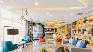 A modern lobby with seating areas, a reception desk, and a bookshelf. - Atour Hotel (Changchun)