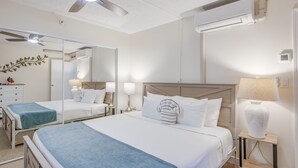 A hotel room with a large bed, two bedside tables with lamps, a ceiling fan, an air conditioning unit, and a mirror. - Direct Oceanfront, unobstructed ocean view top floor penthouse quiet & private.  (Lahaina)