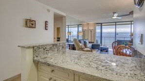 A kitchen with granite countertops, a dining area with a high table and chairs, and a balcony with a view of the ocean. - Direct Oceanfront, unobstructed ocean view top floor penthouse quiet & private.  (Lahaina)