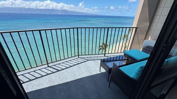 A balcony with a view of the ocean, a small table, and a chair with blue cushions. - Direct Oceanfront, unobstructed ocean view top floor penthouse quiet & private.  (Lahaina)
