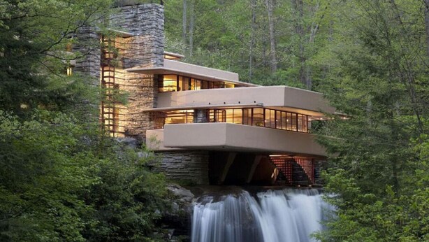 Una casa moderna amb una cascada al davant, envoltada d'arbres.
