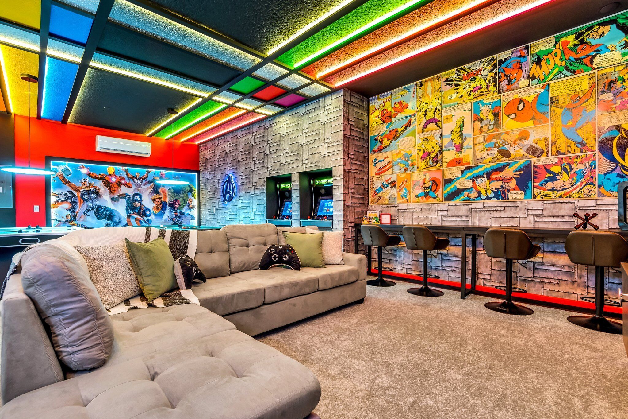 A modern lounge area with a sectional sofa, bar stools, and a vibrant comic book mural on the wall.