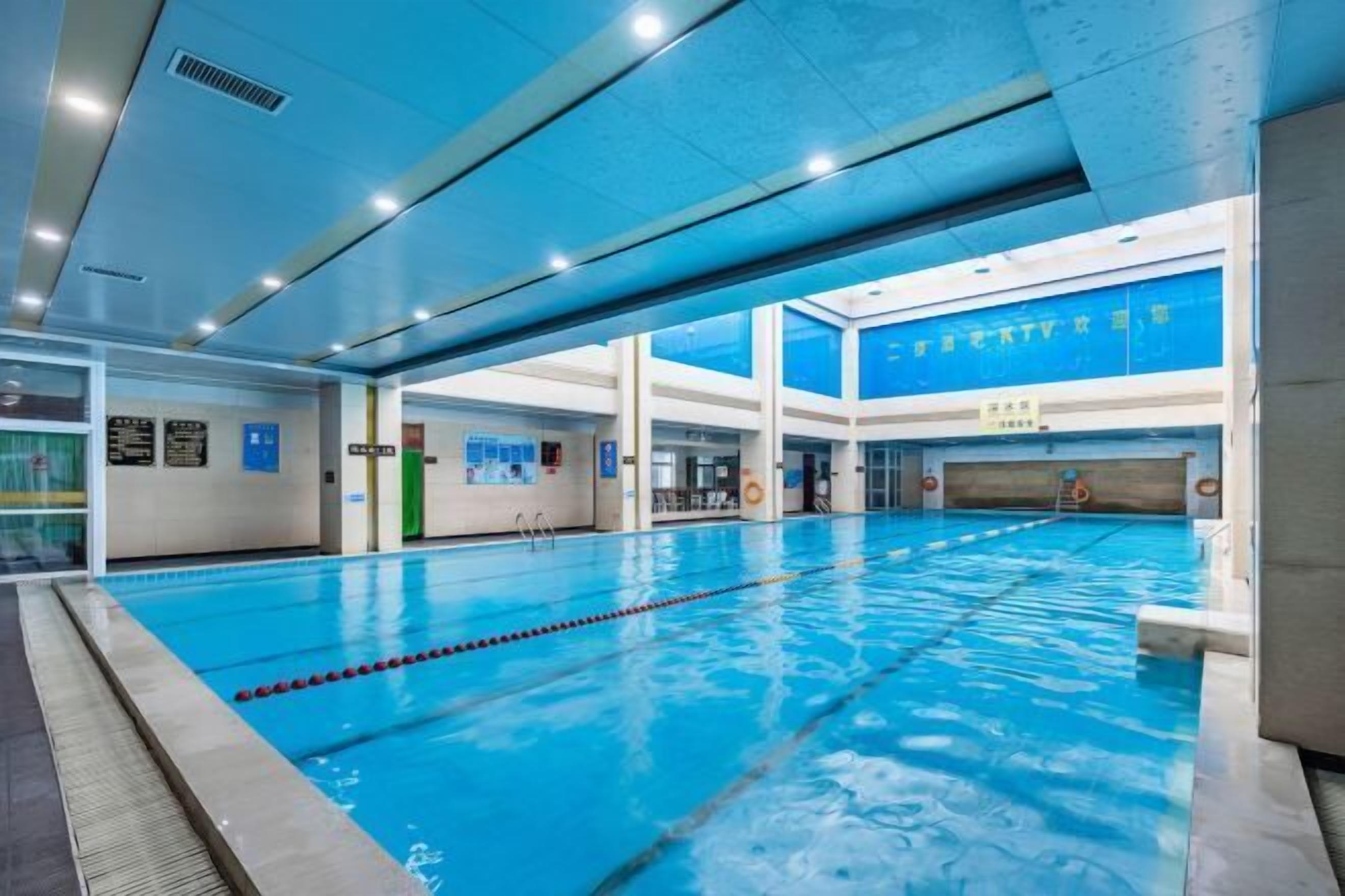 A large indoor swimming pool with clear lanes, surrounded by walls with informational signs and a high ceiling with recessed lighting.