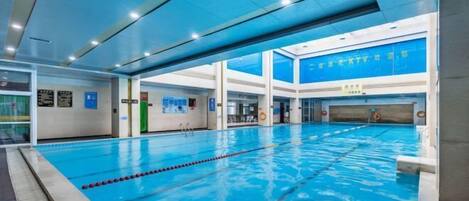 A large indoor swimming pool with clear lanes, surrounded by walls with informational signs and a high ceiling with recessed lighting.