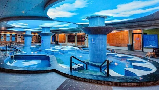 Un espace piscine doté de plusieurs éléments aquatiques et d’un plafond décoré pour évoquer le ciel.