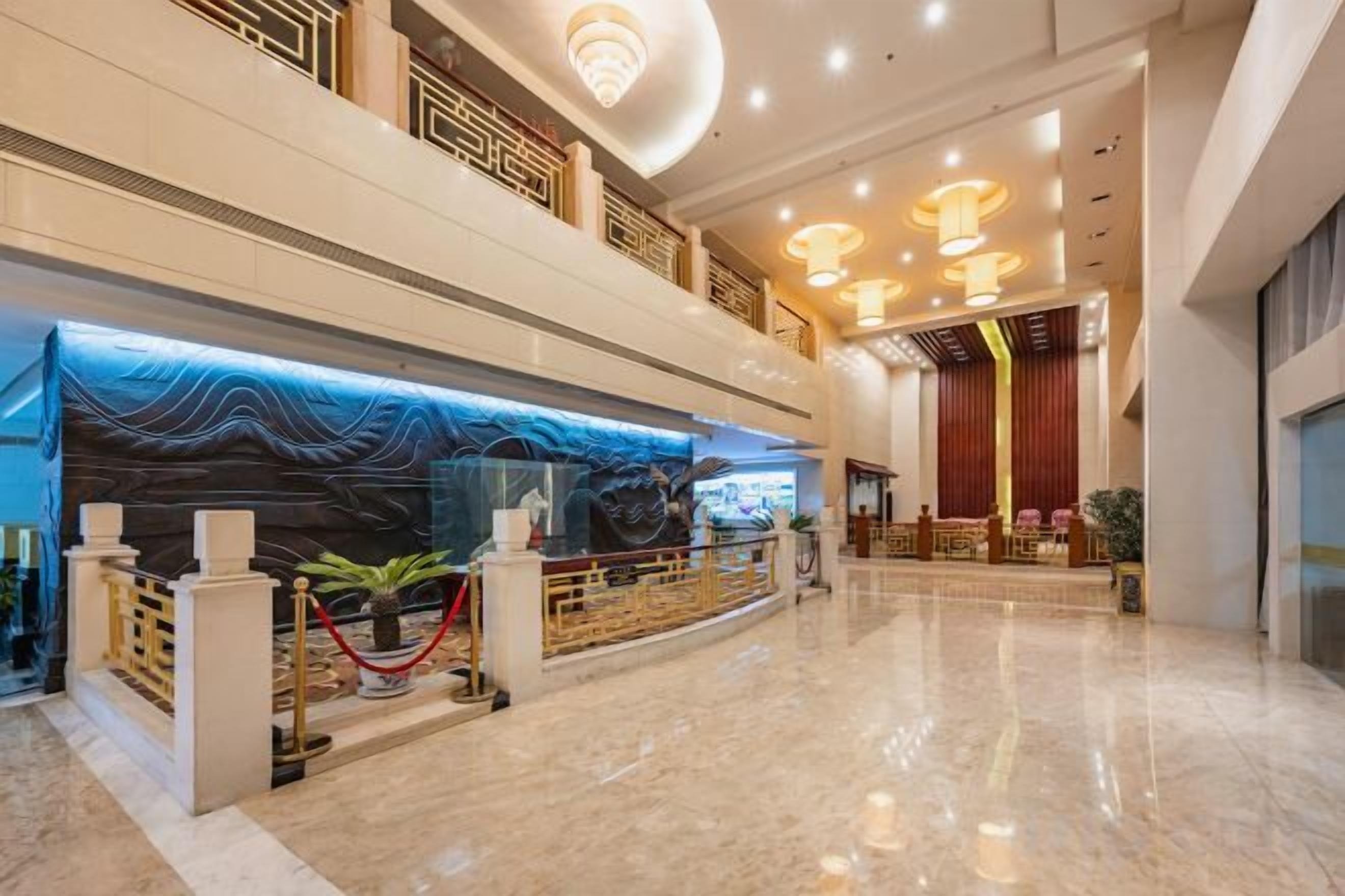 A hotel lobby with a reception desk, a large chandelier, and a high ceiling.