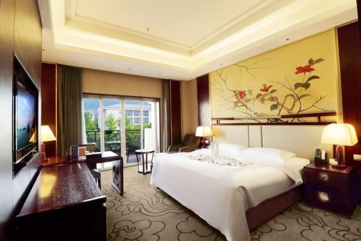 Habitación de hotel con una cama, dos mesitas de noche, un escritorio, una silla, un televisor y un ventanal grande.