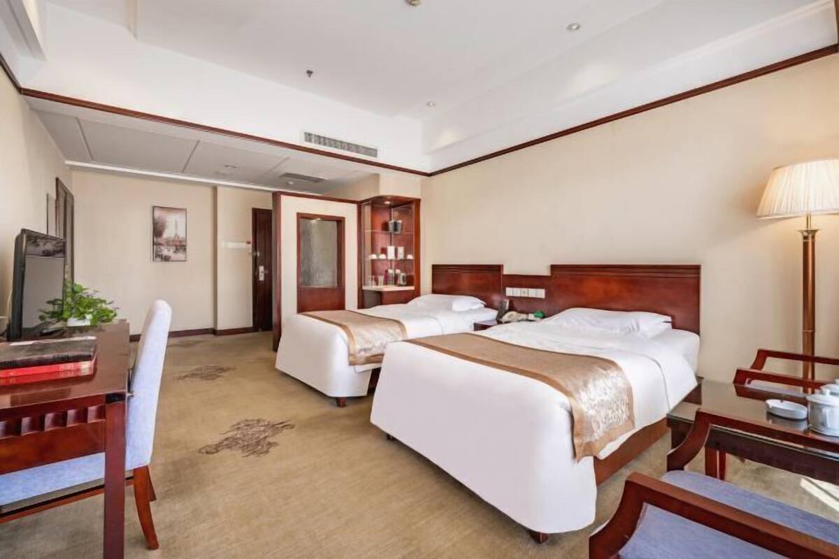 Habitación de hotel con dos camas, un escritorio, una silla, una lámpara y un armario.