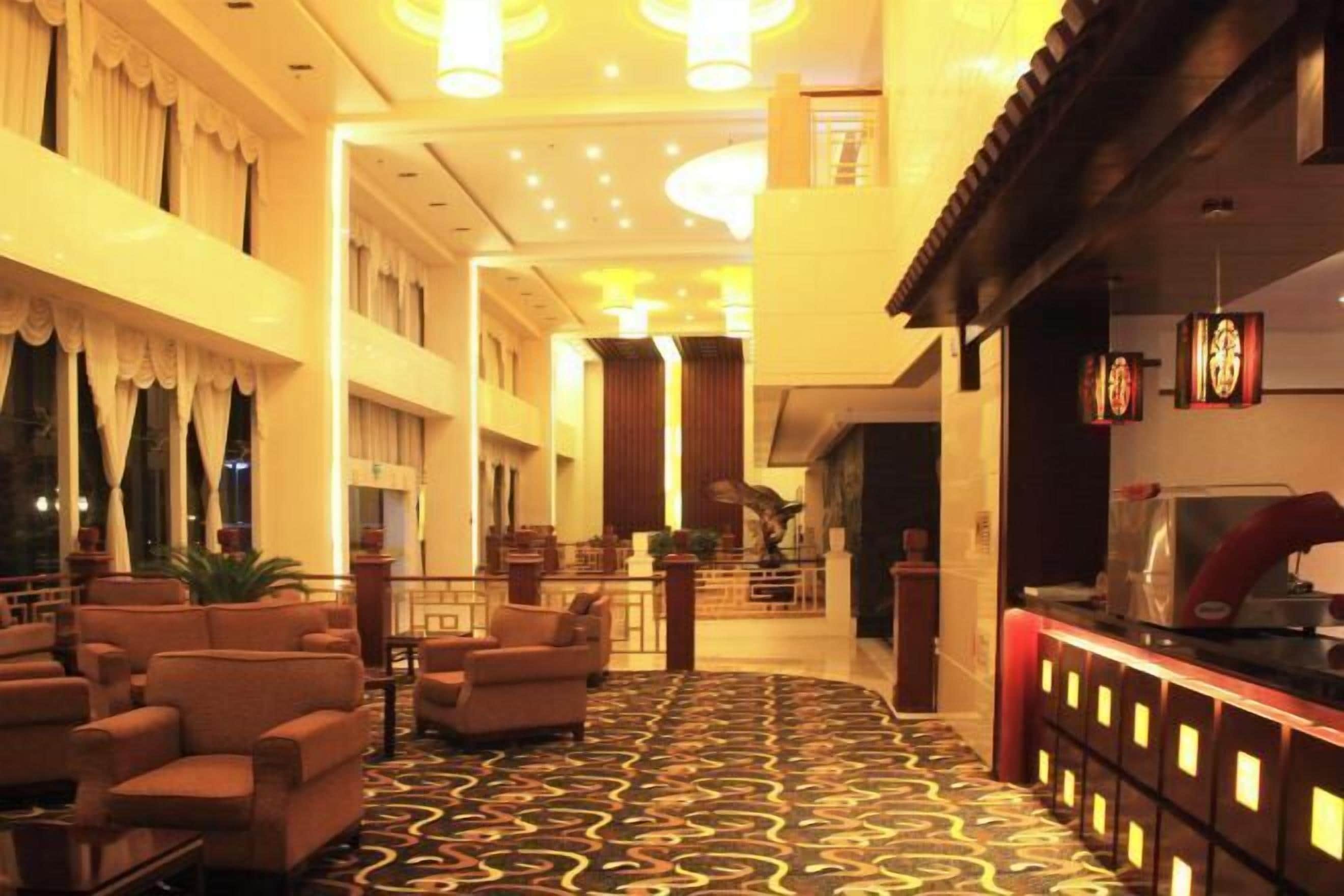 Un vestíbulo de hotel con alfombra estampada, una zona de estar con sofás y un mostrador de recepción.
