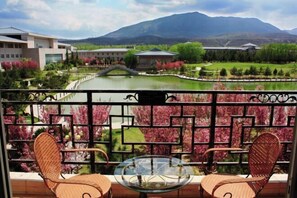 A balcony with wicker chairs and a glass table, overlooking a landscaped garden with a pond and mountains in the background. - Guangcheng Hotel (Pingliang)