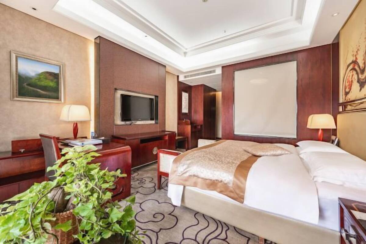 Habitación de hotel con una cama grande, un escritorio con silla, televisión y un ventanal amplio.