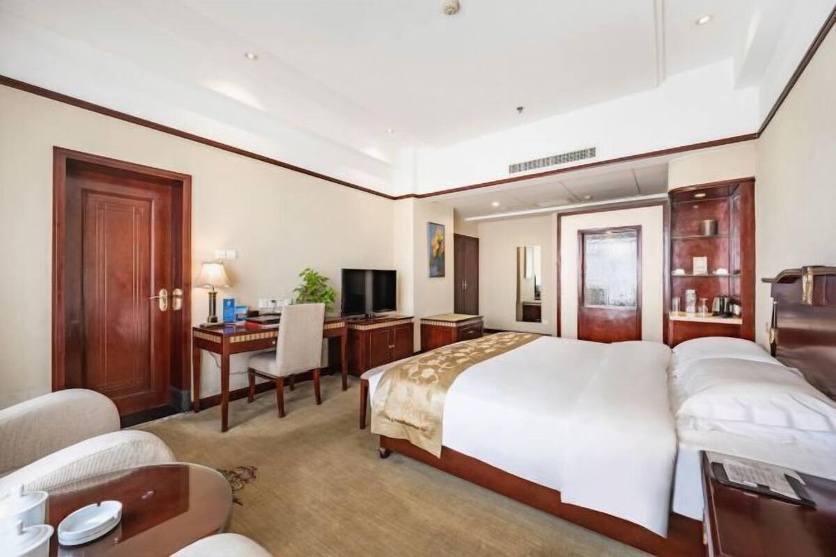 Habitación de hotel con una cama grande, un escritorio con silla, un televisor y una mesita de noche con lámpara.