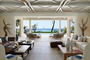 A spacious living room with a view of the ocean, furnished with sofas, chairs, and a coffee table.