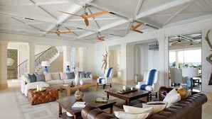 A spacious living area with a high ceiling, multiple seating arrangements, and a view of the outdoors.