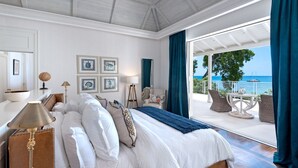 A bedroom with a large bed, a view of the sea, and a balcony with outdoor furniture.