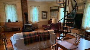 Ein gemütliches Zimmer mit einer Couch, Holzstühlen, einem Esstisch, einem Kamin und einer Wendeltreppe.