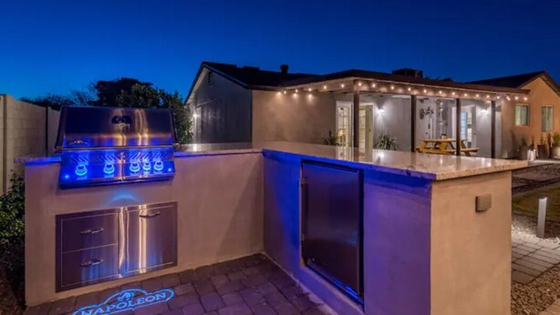 An outdoor kitchen with a built-in grill and lighting, a covered patio area, and a pool. - Modern Farmhouse Living in Phoenix -Prime Location (Phoenix)