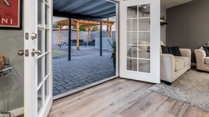 An open sliding glass door leading to an outdoor patio with a pergola, a beige sofa inside, and a framed picture on the wall. - Modern Farmhouse Living in Phoenix -Prime Location (Phoenix)