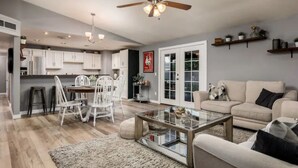A modern living room with a glass coffee table, a beige sofa, and a dining area with white chairs.