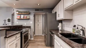A modern kitchen with white cabinets, granite countertops, stainless steel appliances, and a wooden floor.