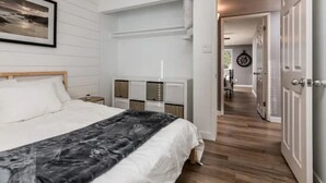 A bedroom with a bed, a nightstand, a dresser, and a hallway leading to another room.