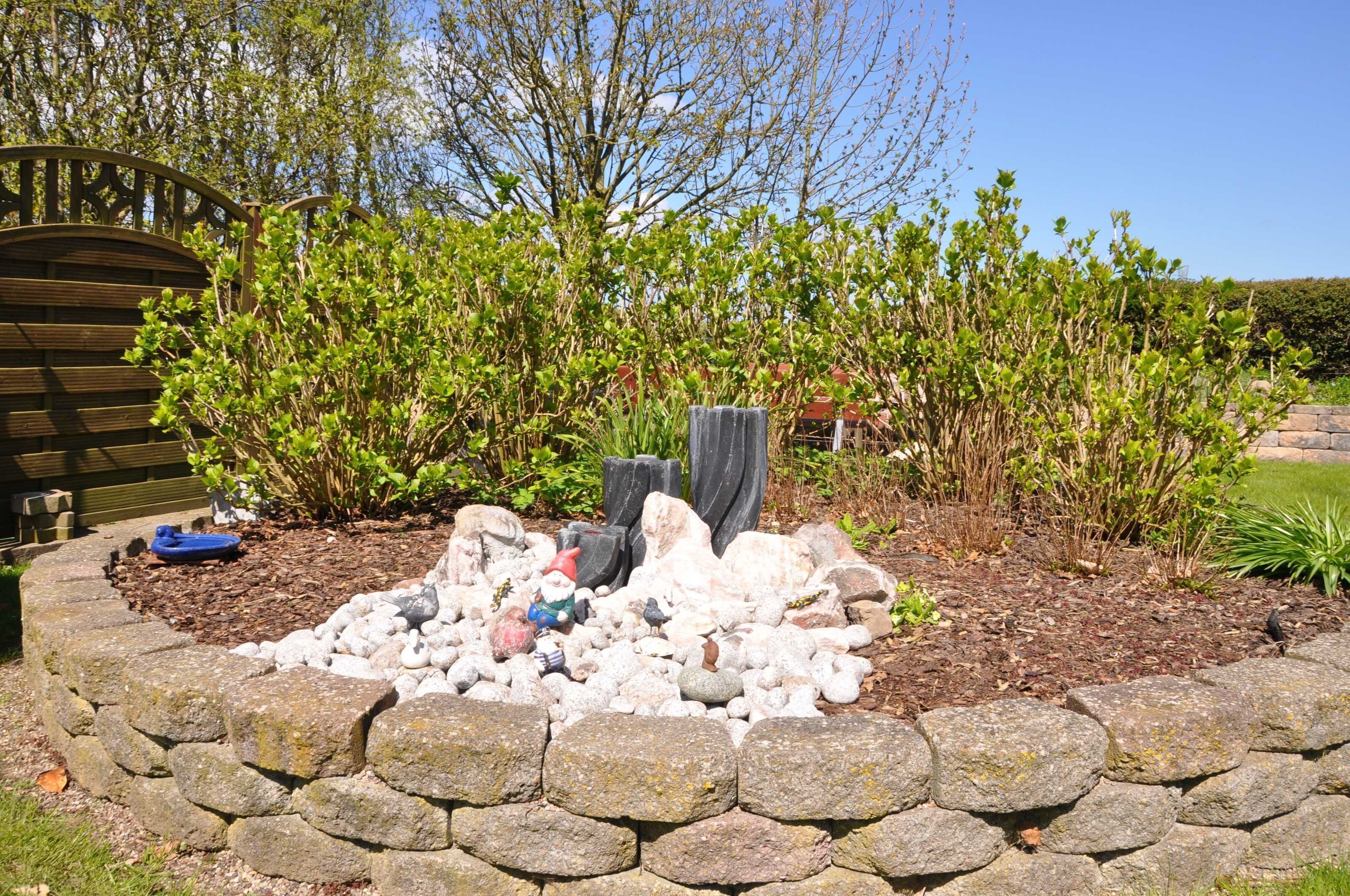 Een tuin met een stenen muur, een houten bankje en diverse planten.
