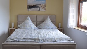 Une chambre à coucher avec un lit, deux tables de chevet, un tableau au mur et une fenêtre avec des rideaux.