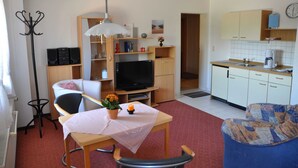 Un espace de vie compact comprenant une table à manger, un téléviseur, un canapé, un coin cuisine et un porte-manteau.