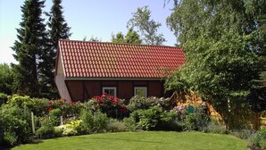 Une maison avec un toit recouvert de tuiles rouges, entourée d’un jardin bien entretenu où poussent différentes plantes et fleurs.