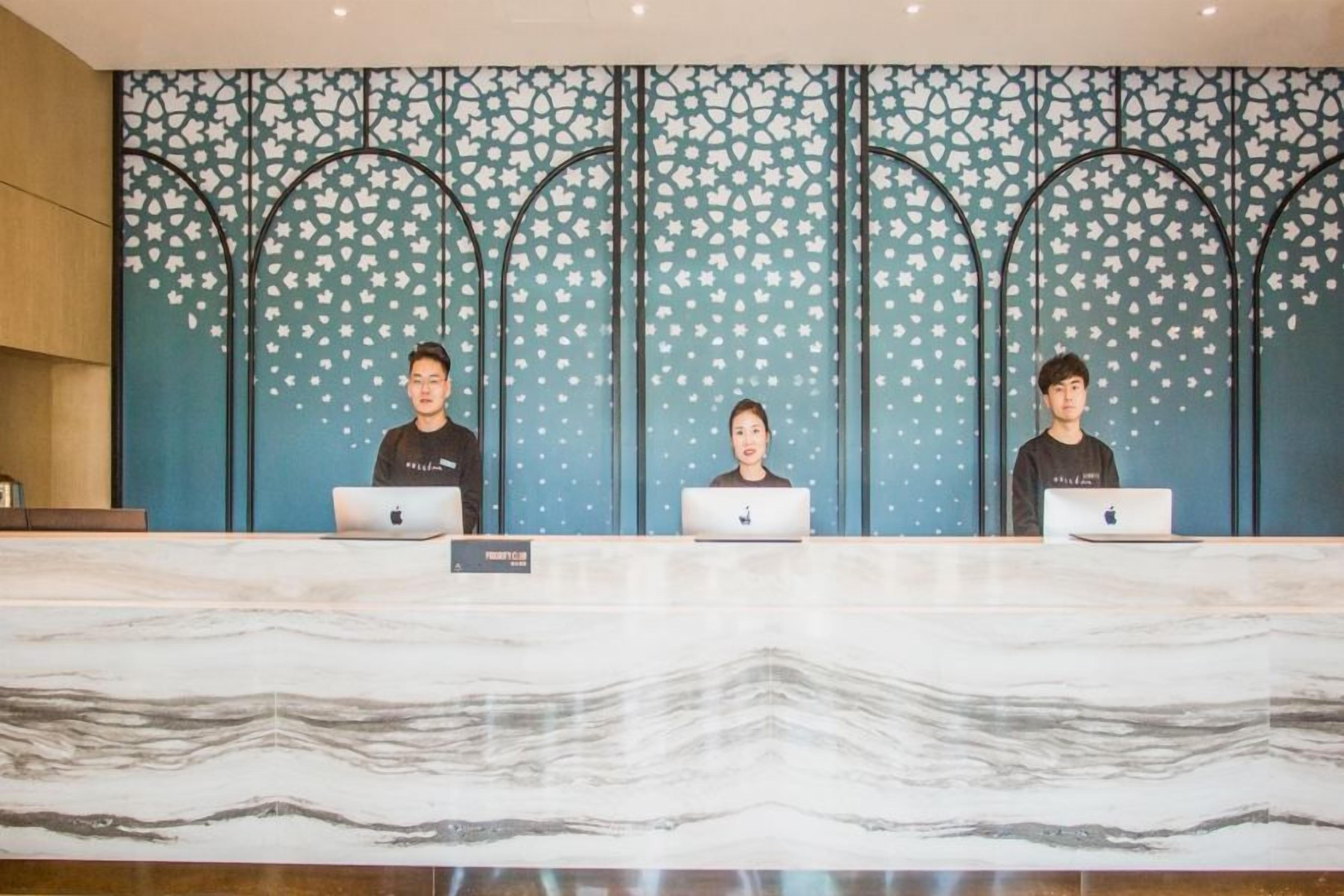 Tres personas sentadas en un mostrador de recepción con portátiles, un suelo con diseño de mármol y una pared decorativa con un motivo estelar.