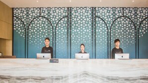 Drie personen zitten aan een receptiebalie met laptops, een vloer met een marmerlook en een decoratieve wand met een stervormig patroon.