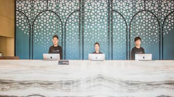 Tres personas sentadas en un mostrador de recepción con portátiles, un suelo con diseño de mármol y una pared decorativa con un motivo estelar.