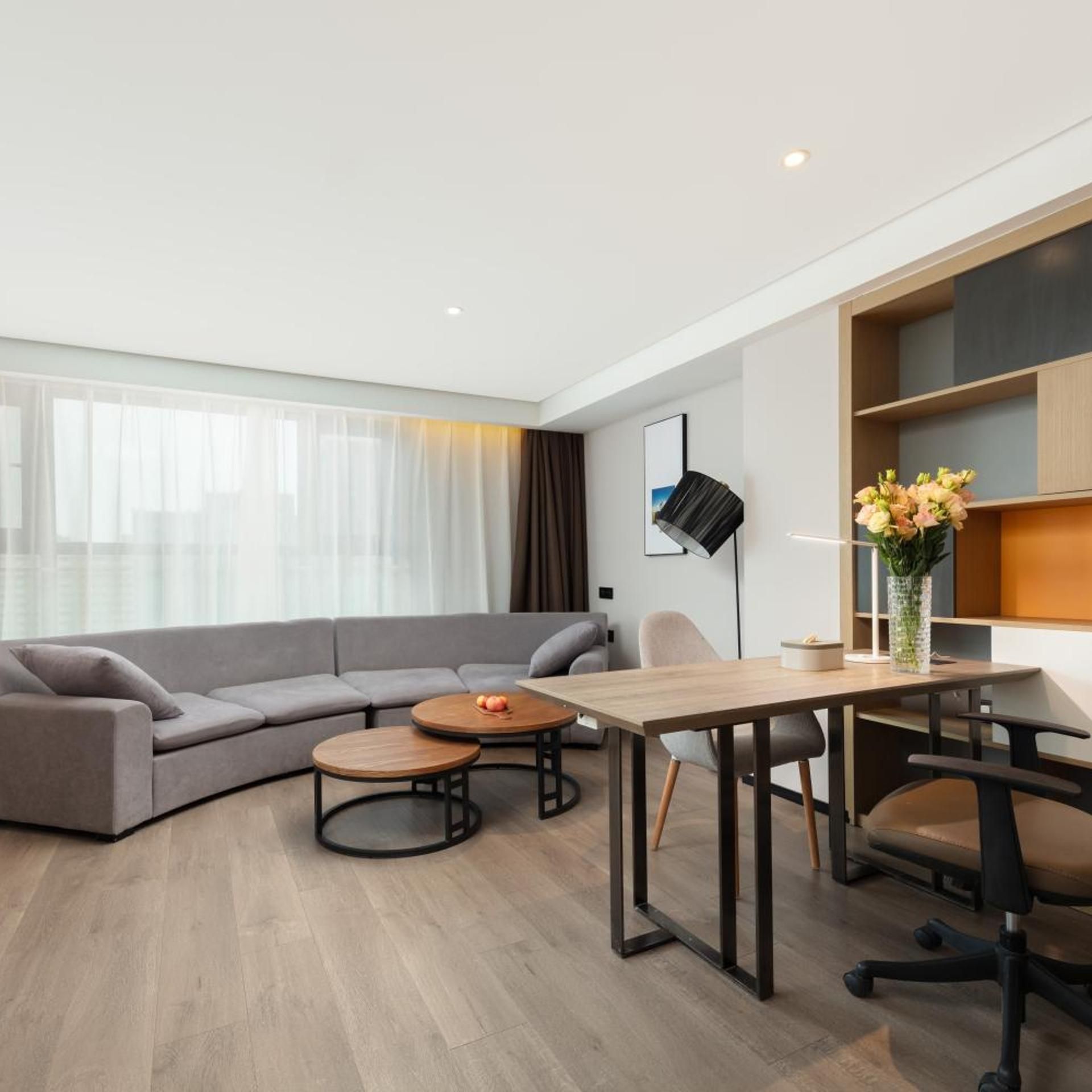 Una sala de estar moderna con un sofá seccional gris, una mesa de centro de madera, una mesa de comedor con sillas y una lámpara de pie.