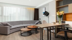 Een moderne woonkamer met een grijze hoekbank, een houten salontafel, een eettafel met stoelen en een vloerlamp.