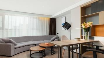Una sala de estar moderna con un sofá seccional gris, una mesa de centro de madera, una mesa de comedor con sillas y una lámpara de pie.