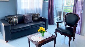 Ein Wohnzimmer mit einer schwarzen Ledersofa, einem Holzstuhl und einem kleinen Tisch mit einer Vase voller gelber Blumen.