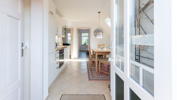 A narrow kitchen with white cabinets, a dining area with a wooden table and chairs, and a view through a glass door.