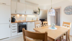 A modern kitchen with white cabinetry, a microwave, and a dining area with a wooden table and chairs.